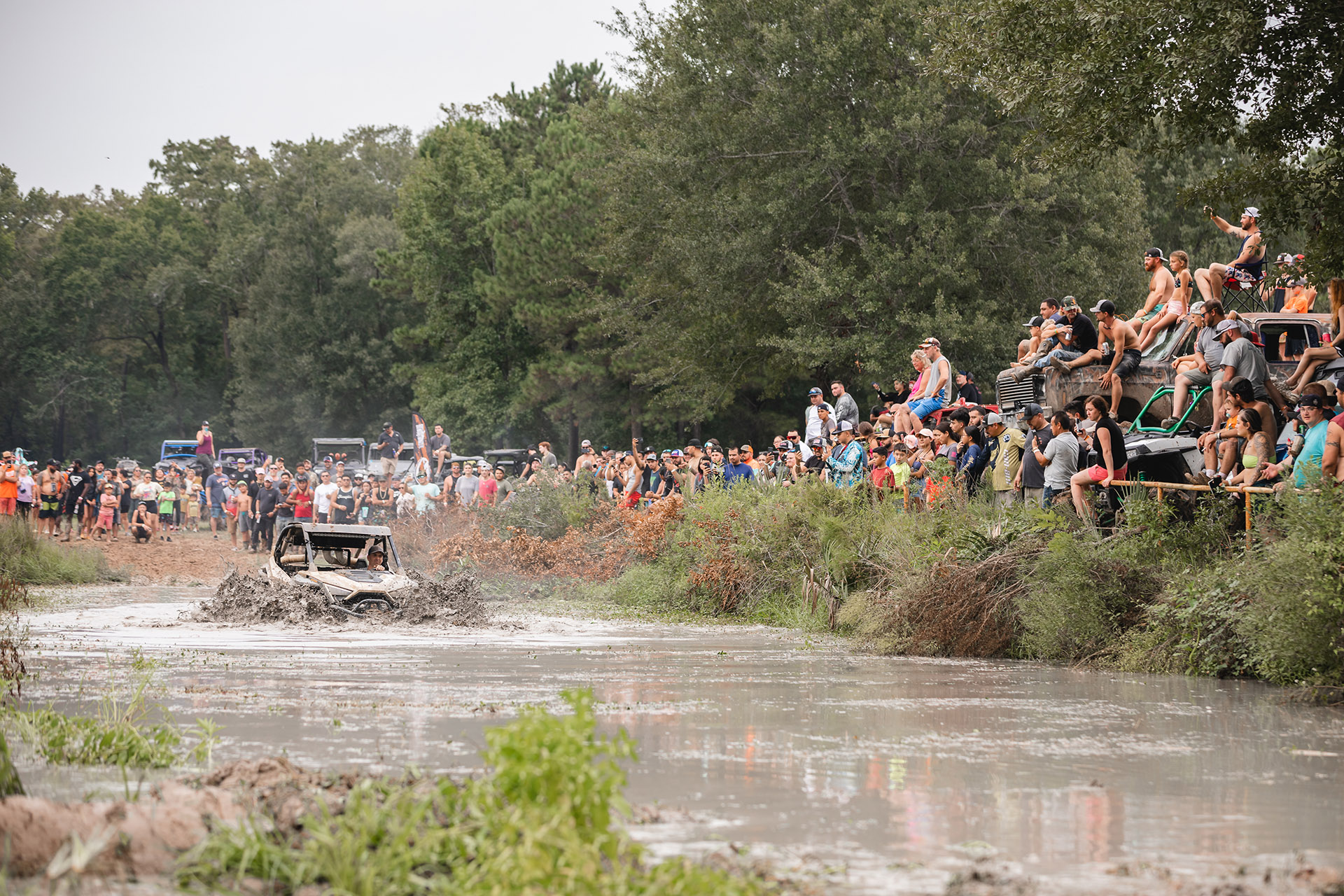 Off-road vehicle splashing through the water in front of the trail crowd